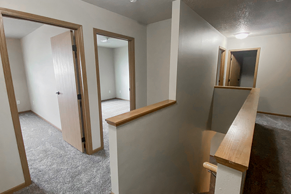 View from the top of the staircase in Osgood Townhome with views of all three bedrooms, bathroom door, carpet, and top landing