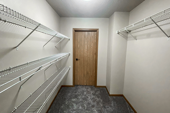 Walk-through closet in Osgood Townhome with shelves, bathroom door, and carpet flooring