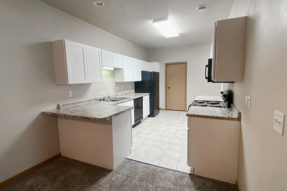 Full kitchen in Osgood Townsite, Fargo ND with vinyl floor, access to bathroom and garage, storage, cupboards, open fridge, and microwave