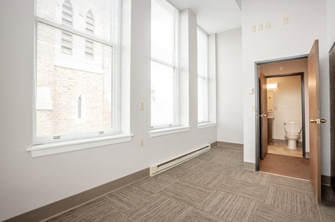 a bedroom with three large windows and a bathroom with a toilet