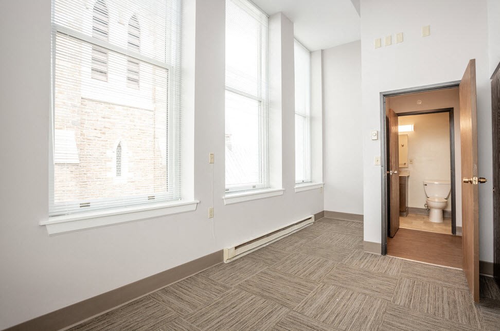 a bedroom with three large windows and a bathroom with a toilet