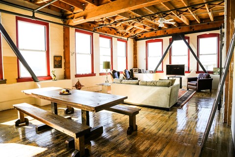 A wooden table and benches are in a room with a high ceiling and large windows.