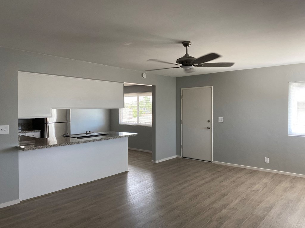 an empty living room with a kitchen and a ceiling fan