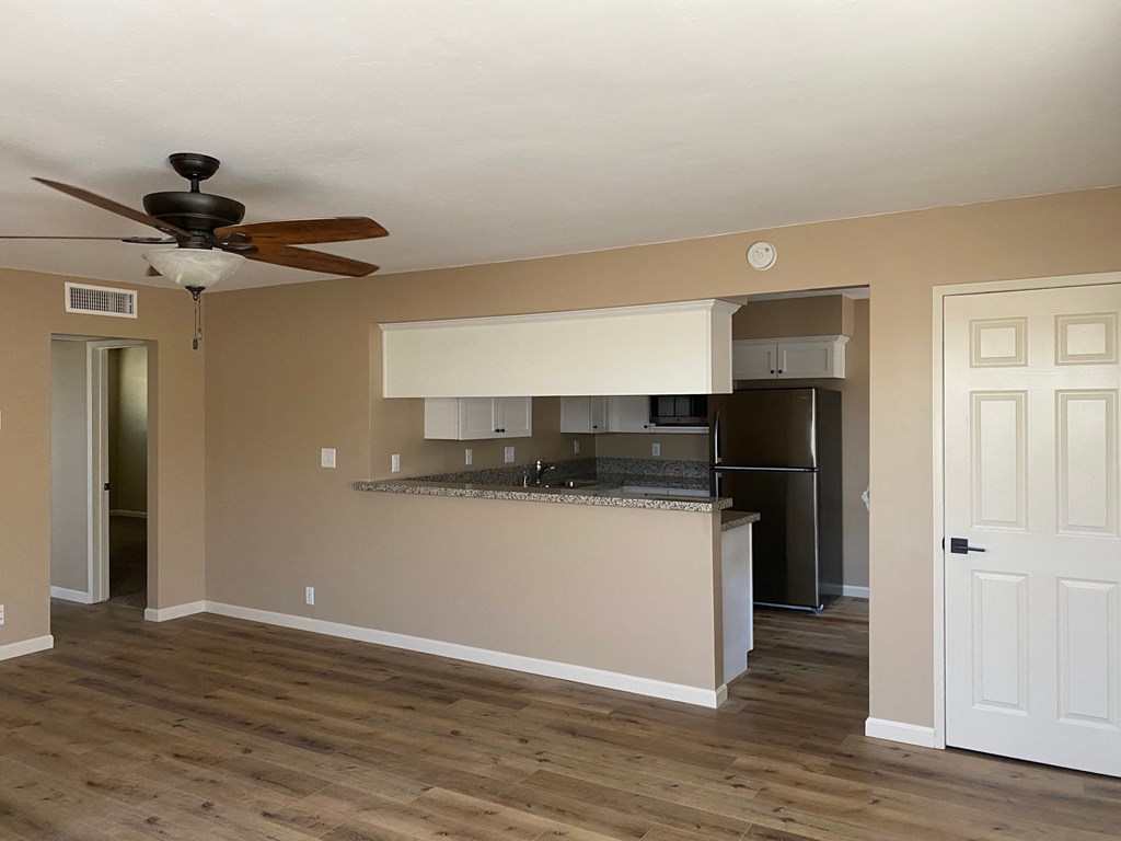 an empty living room with a kitchen and a ceiling fan