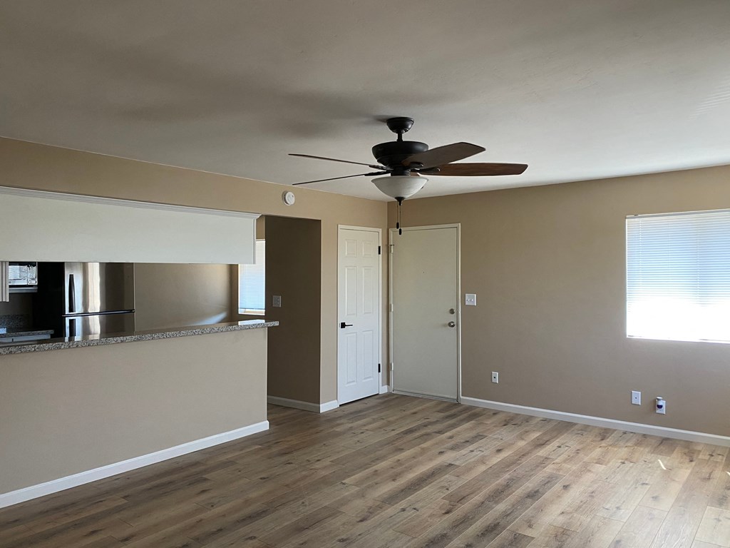 an empty living room with a ceiling fan and a kitchen