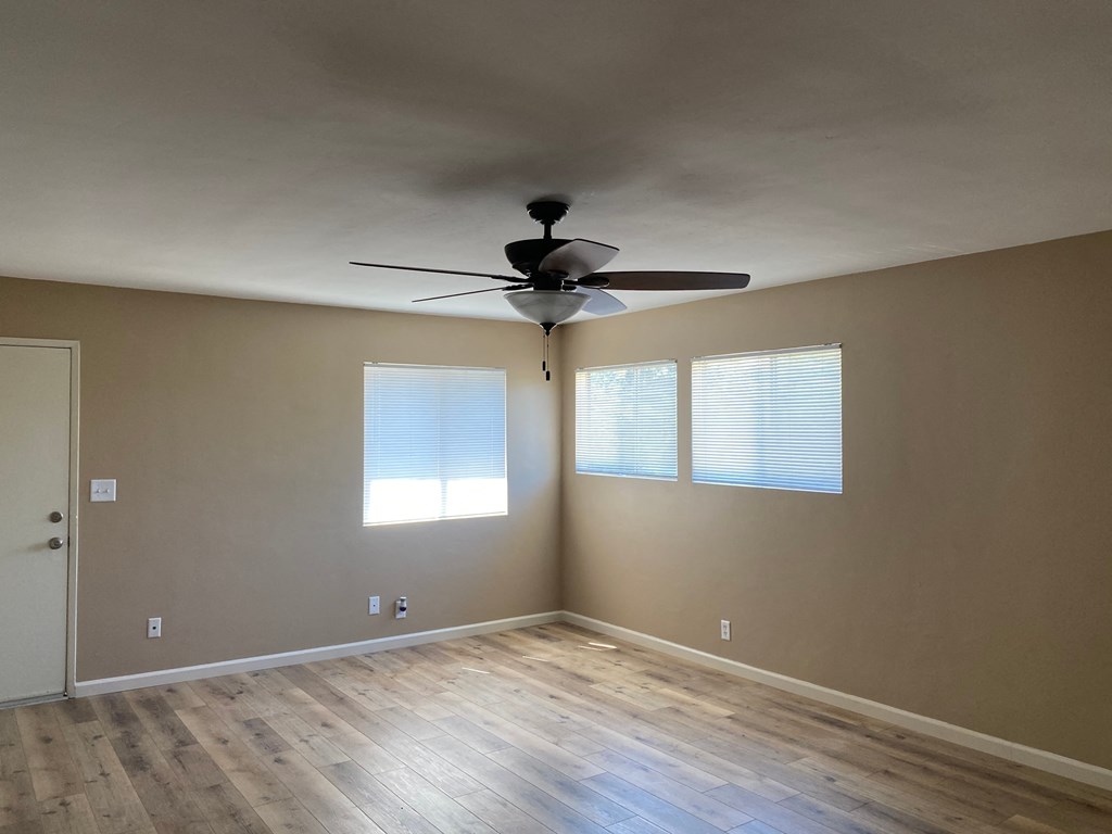 an empty living room with a ceiling fan and windows