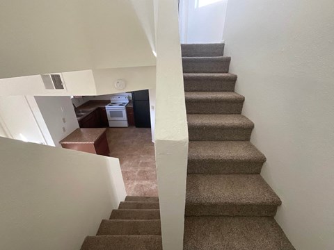 a view from the top of the stairs looking down into the living room and kitchen