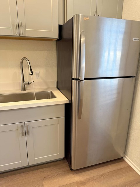 A stainless steel refrigerator stands in a kitchen with white cabinets.