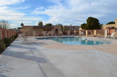 A large outdoor swimming pool surrounded by a concrete patio and a red brick wall.