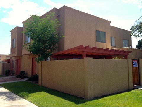 A tan house with a red awning and a tree in front.