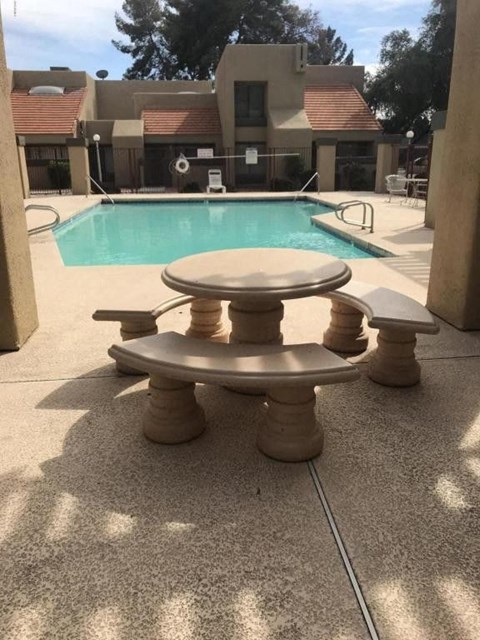 A concrete table and chairs are in the foreground of a pool area.