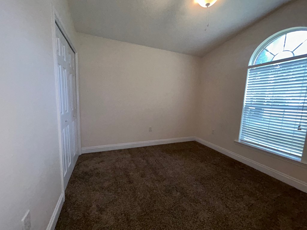 A room with a carpeted floor and a window with blinds.