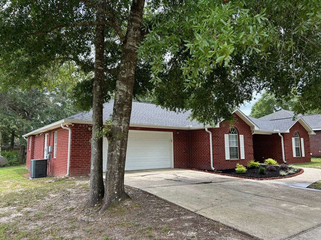 A red brick house with a white garage door and a tree in front.