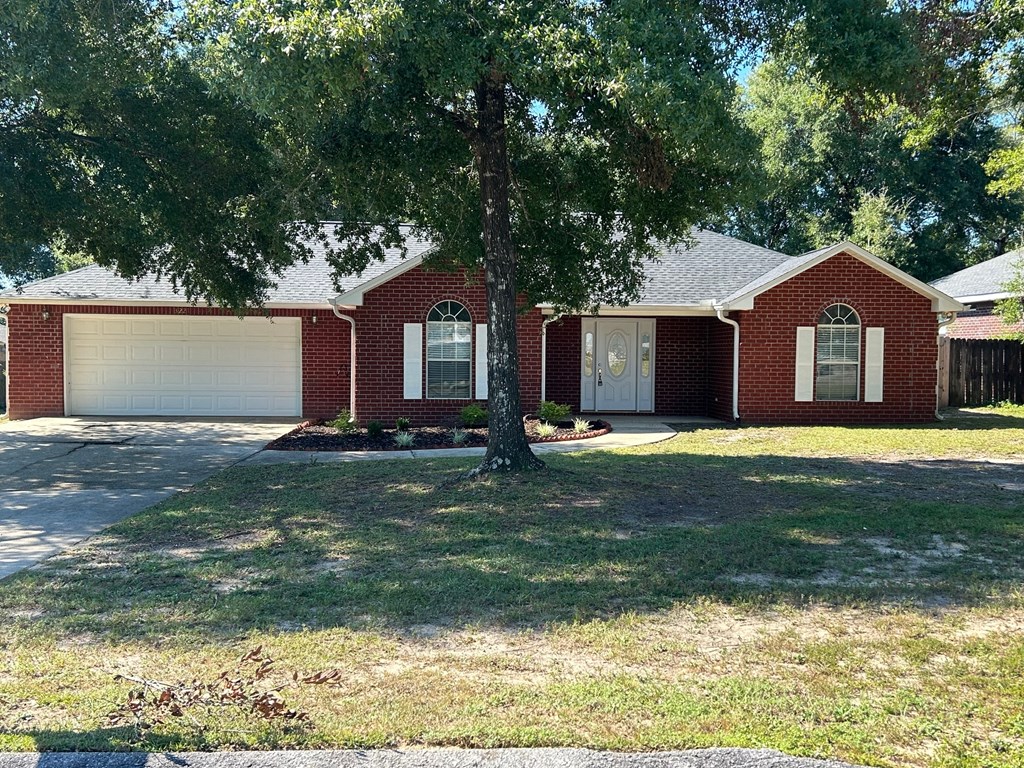A red brick house with a white garage door and a tree in front.