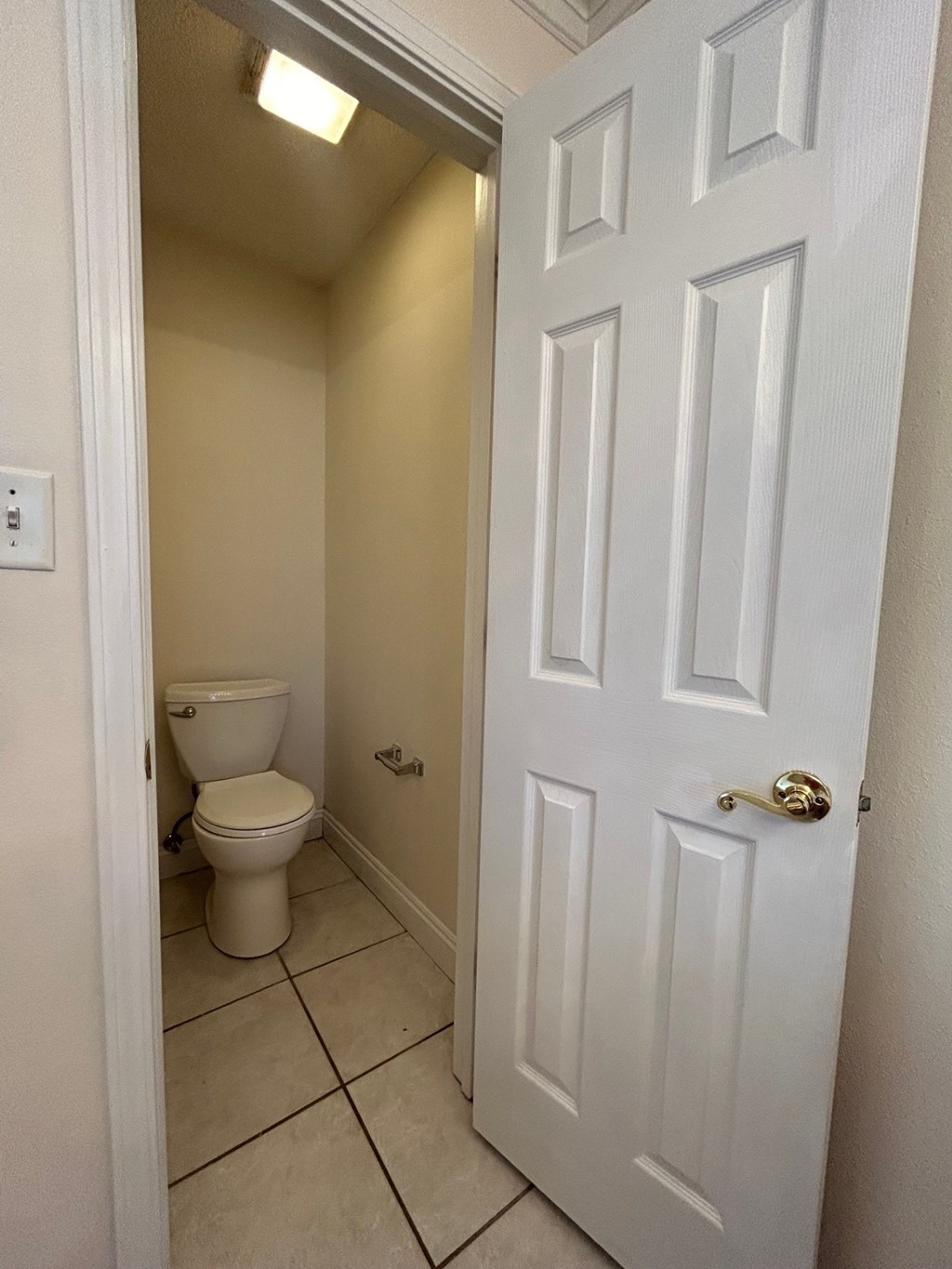 A white door is open to a small bathroom with a toilet.