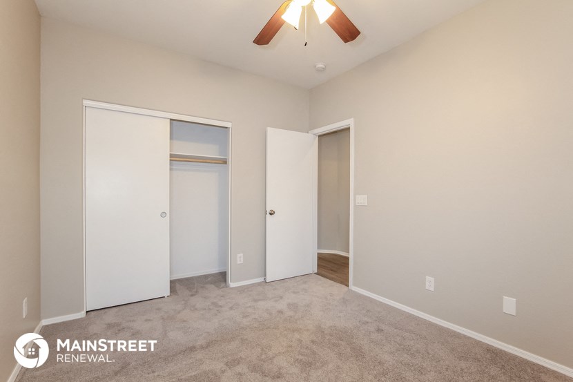 the spacious living room with carpeted flooring and a ceiling fan