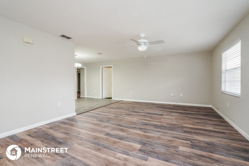 the spacious living room with wood flooring and a ceiling fan