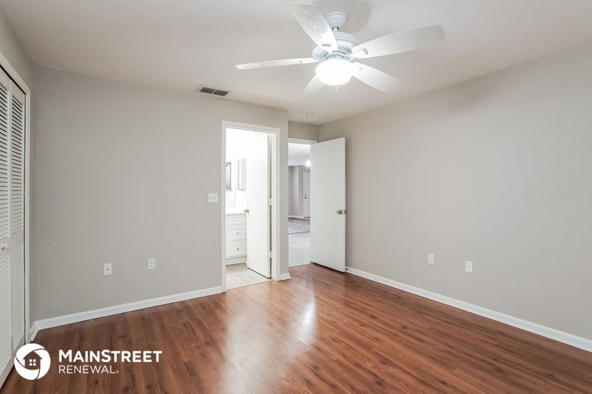 the spacious living room with wood flooring and a ceiling fan