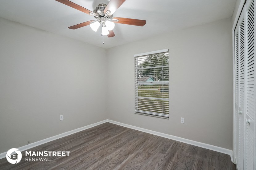 the spacious living room has a ceiling fan and wood flooring