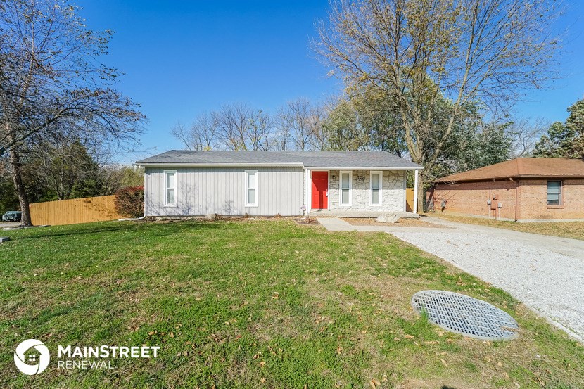 a small white house with a yard and a red door
