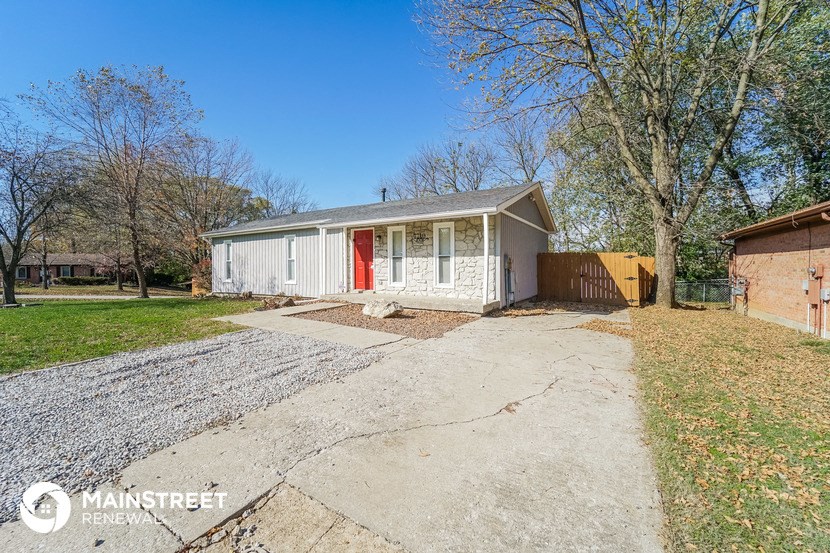 a small white house with a driveway and a red door