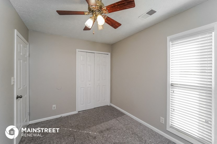 the spacious bedroom of this manufactured home has a ceiling fan and a white door