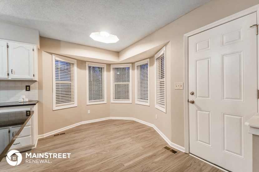 an empty living room with a white door and a kitchen
