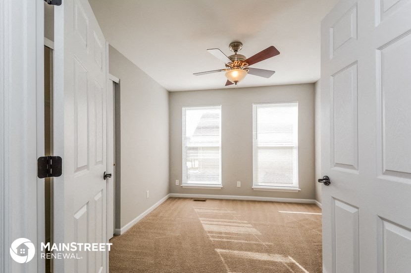 an empty room with a ceiling fan and two windows