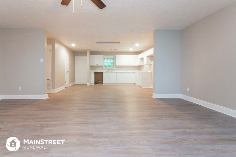 an empty living room and kitchen with wood floors and a ceiling fan