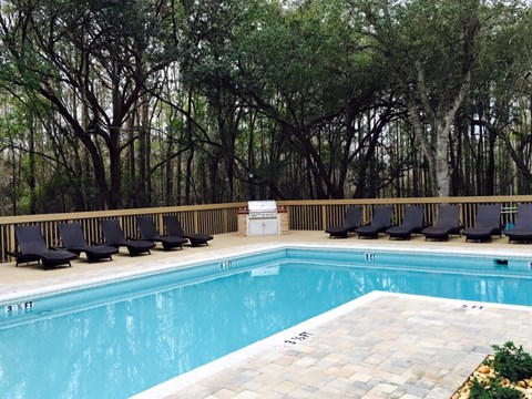 A pool surrounded by trees and lounge chairs.