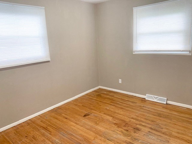 an empty room with a wooden floor and two windows