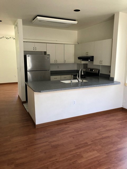 A kitchen with a stainless steel refrigerator and wooden floors.