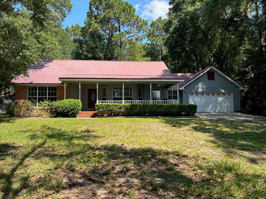 A house with a red roof and white walls is surrounded by greenery.