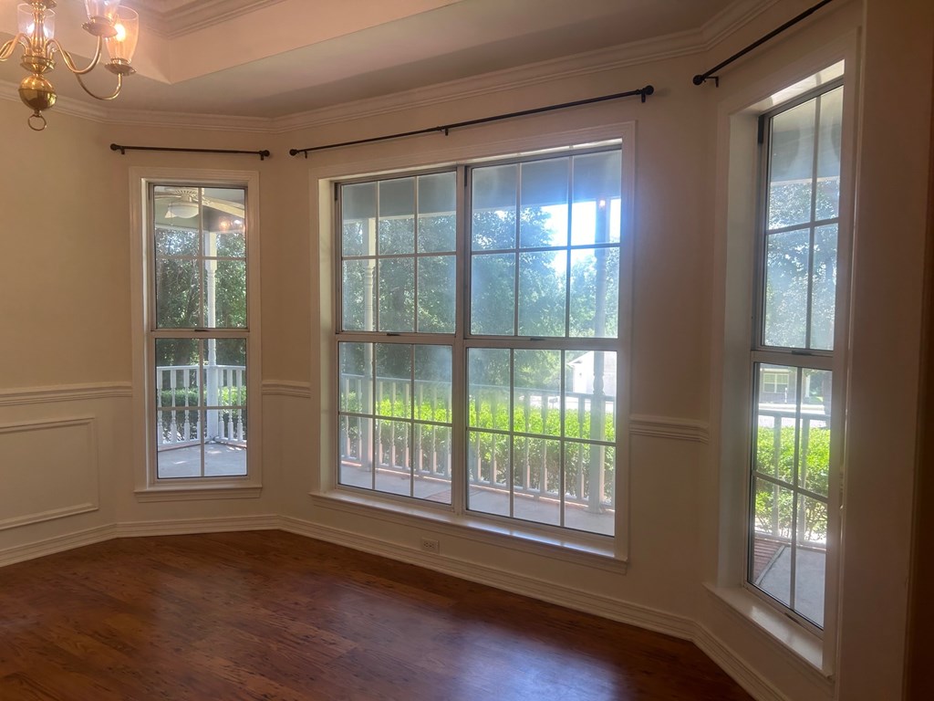 A room with a chandelier, three windows, and a wooden floor.