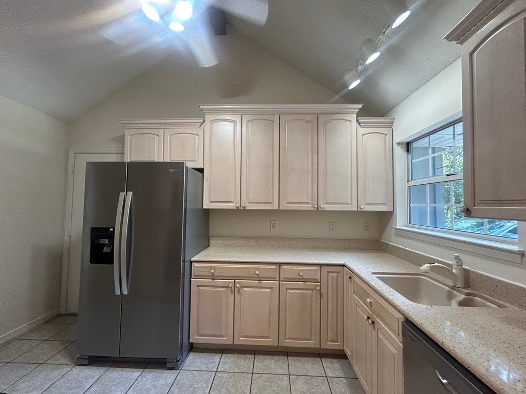A kitchen with a refrigerator, cabinets, and a window.