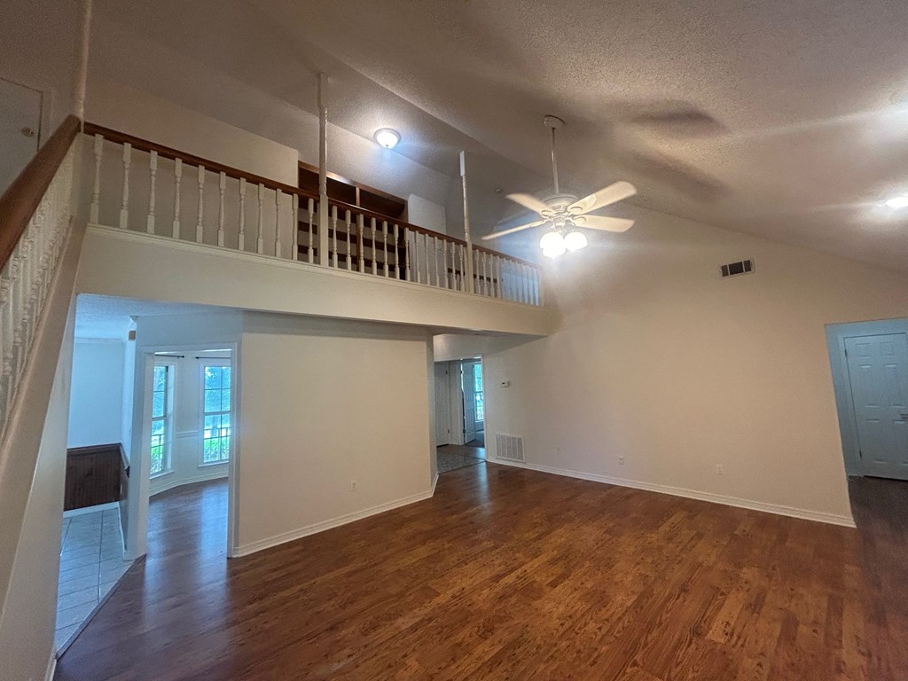 A spacious room with wooden floors and a ceiling fan.