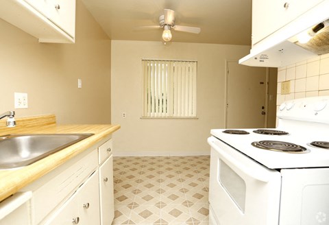 A kitchen with a white stove top oven and a white tiled floor.
