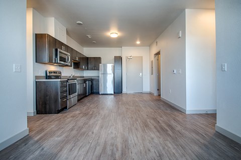 an empty living room with a kitchen with stainless steel appliances