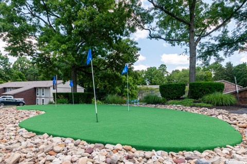 a putting green with three flags on it in front of a house