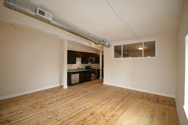 an empty living room with a wood floor and a kitchen