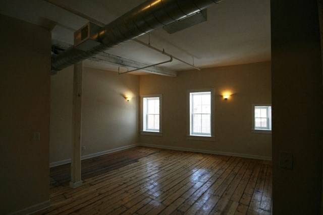 an empty room with a wooden floor and three windows