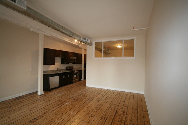 an empty living room with a wood floor and a kitchen