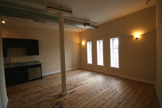 an empty living room with wooden floors and a kitchen