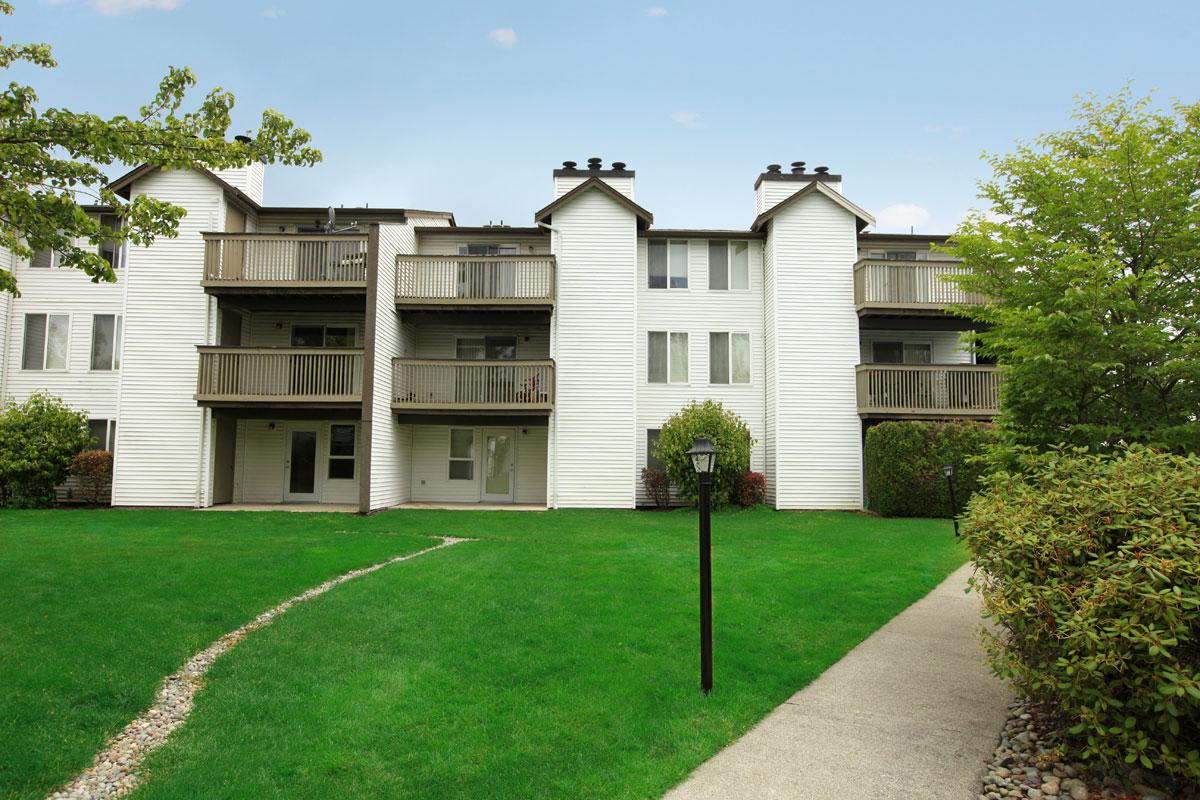 an apartment building with a green lawn and a sidewalk