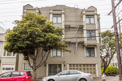A grey two-story building with a tree in front of it.