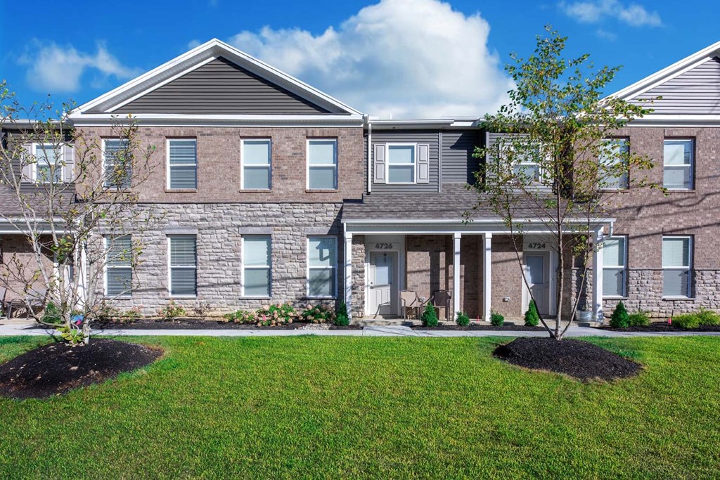 the front of a brick house with a lawn and a tree