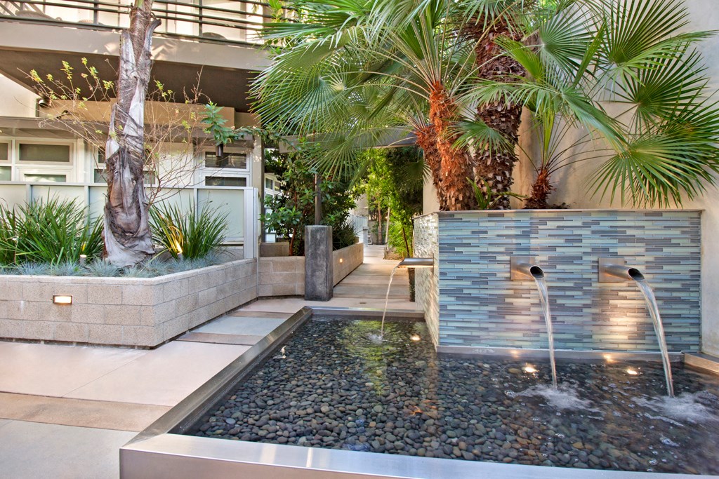 a pool with a waterfall in a courtyard with palm trees