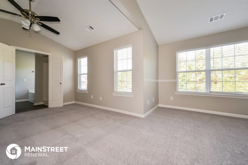 the spacious living room with ceiling fan and large windows