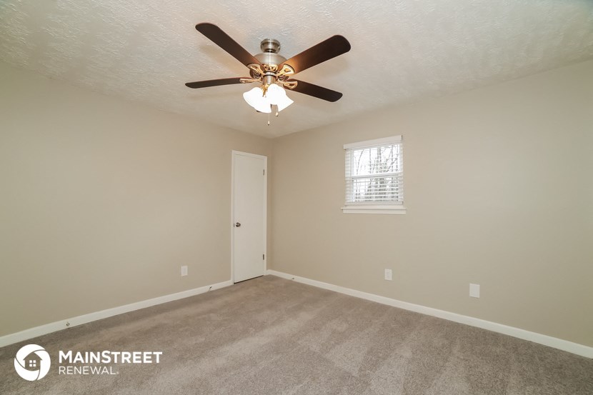 the spacious living room with ceiling fan and carpeting