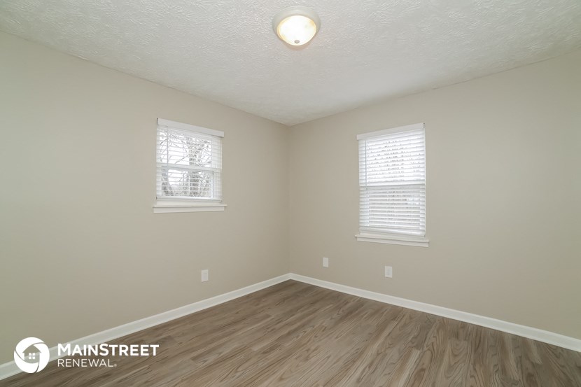 the interior of an empty room with wood flooring and two windows